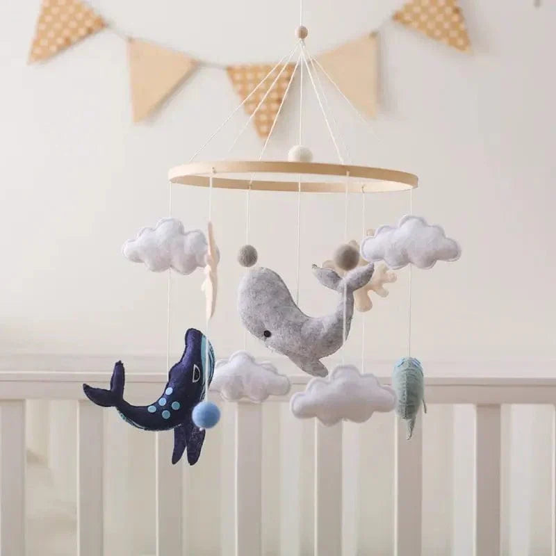 Ocean baby mobile with whales and clouds hanging above a crib beneath triangular bunting
