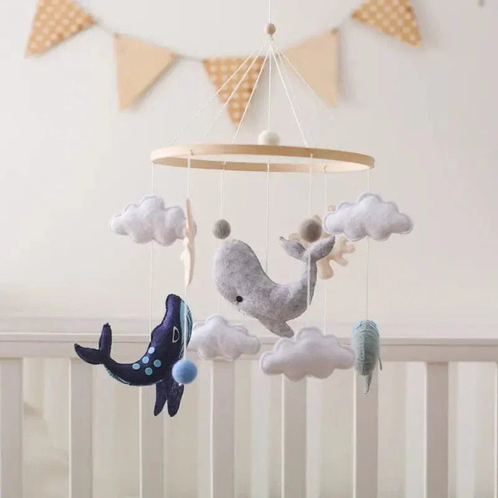 Ocean baby mobile with whales and clouds hanging above a crib beneath triangular bunting