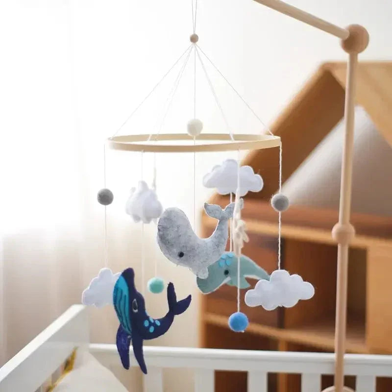 Ocean baby mobile with whales and clouds suspended from a wooden mounting arm beside a crib