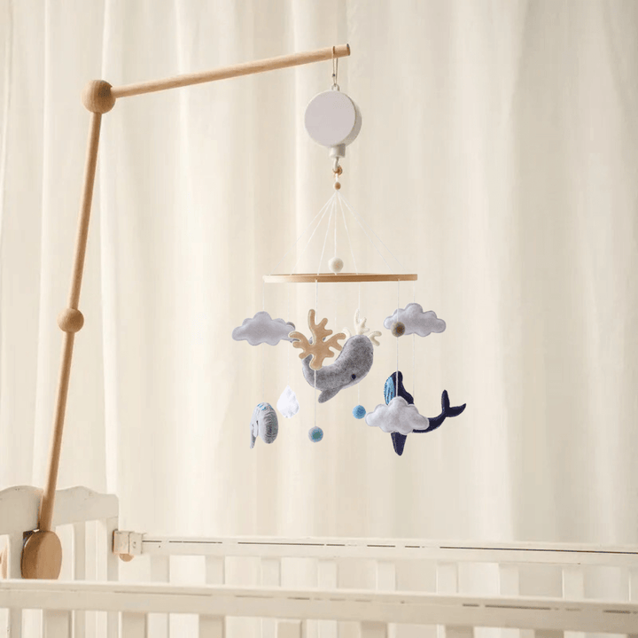 Ocean whale-and-cloud baby mobile hanging from a wooden arm above a white crib