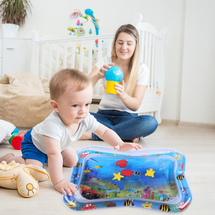 Baby leaning over an ocean-themed water mat with an adult seated behind