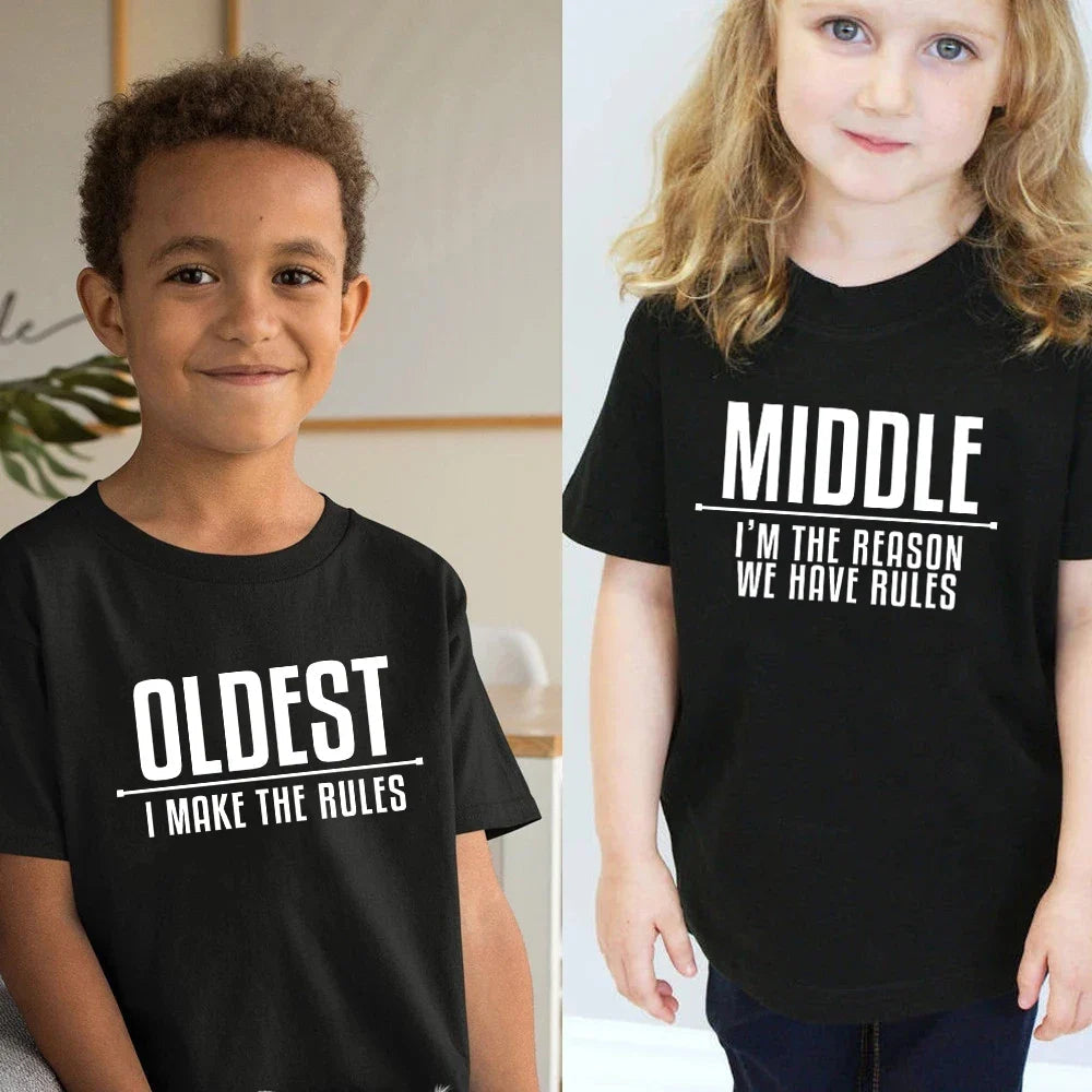 Two children wearing black Oldest and Middle T-shirts with white family-role slogans.