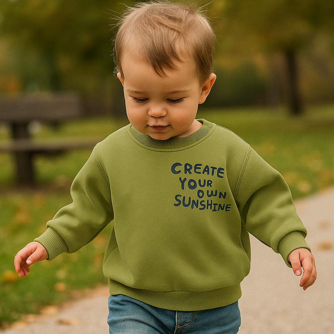 Child wearing an olive green sunshine sweatshirt with jeans on an outdoor path.