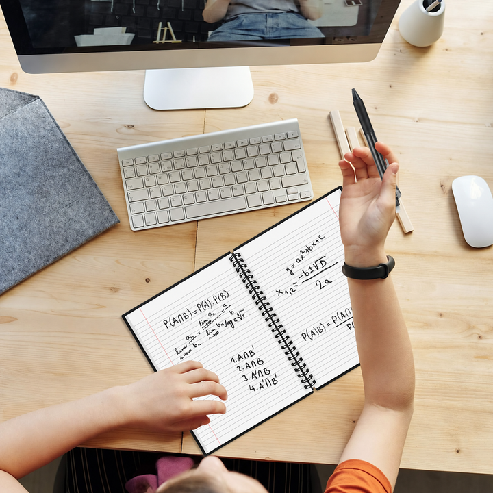 Open spiral notebook with handwritten notes beside a keyboard on a wooden desk
