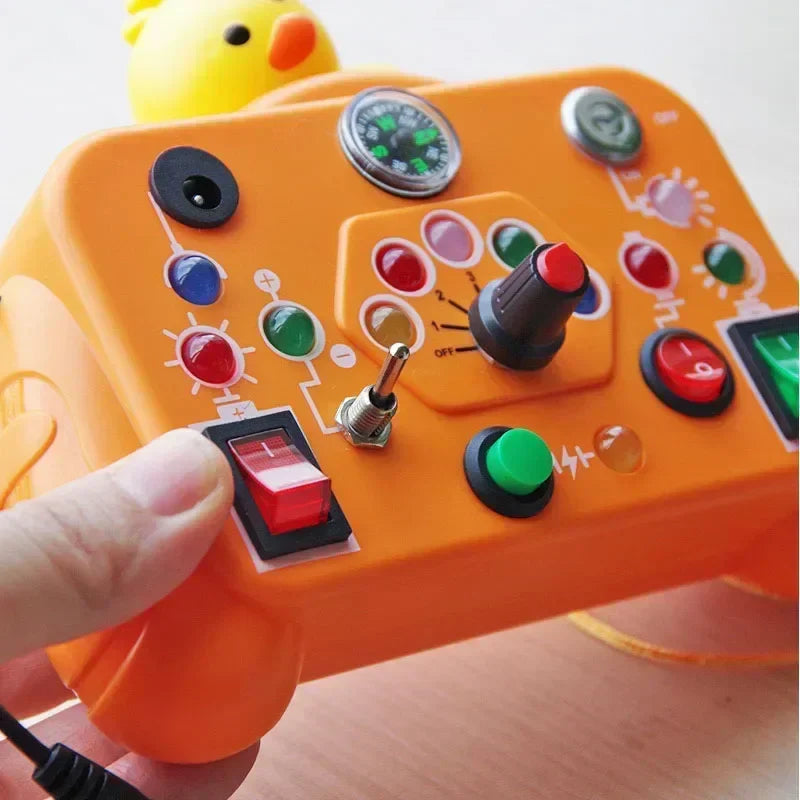 Hand pressing a red rocker switch on an orange activity board with a yellow duck topper