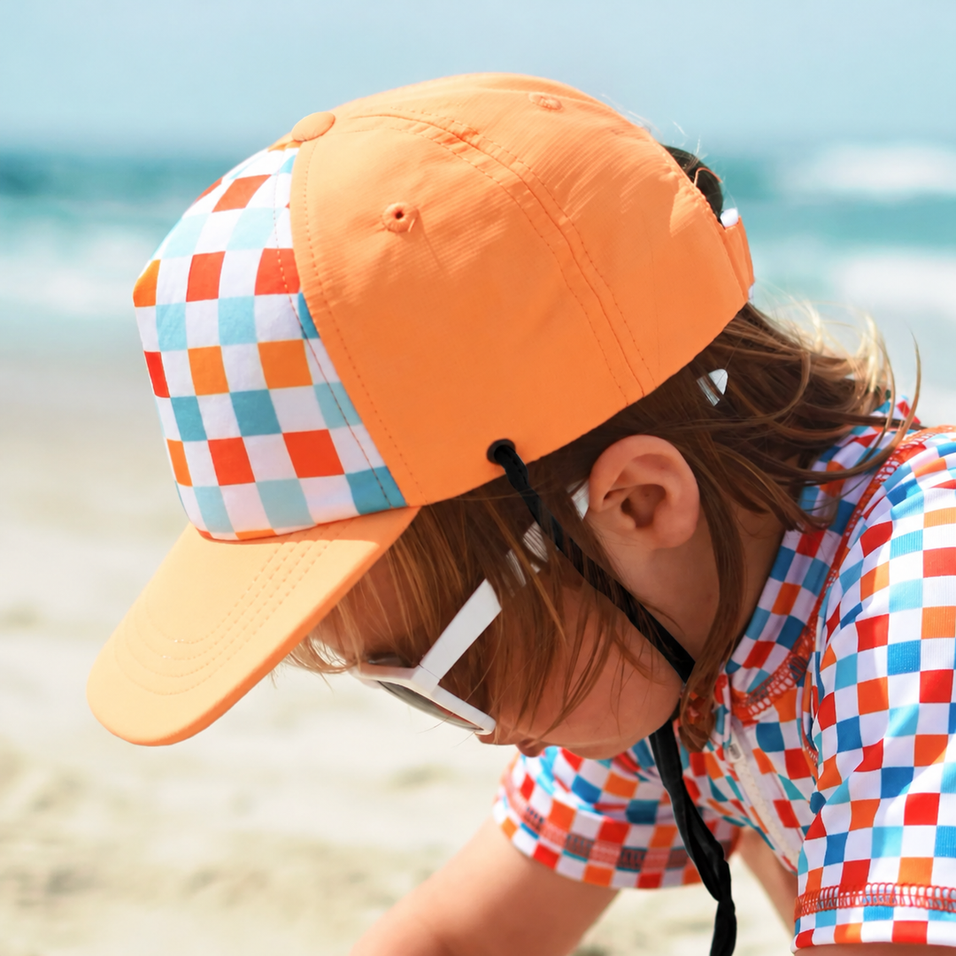 Child wearing an orange cap with a multicolor checkerboard front and flat brim