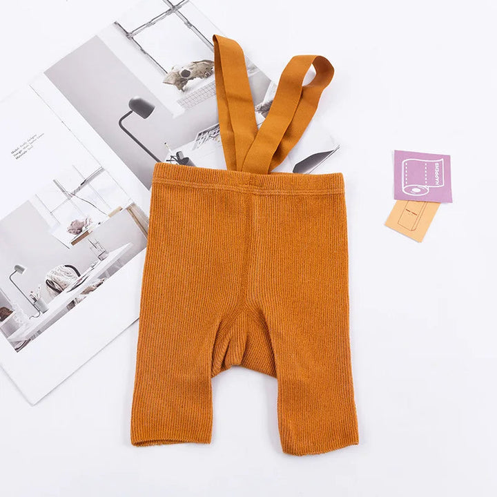Orange ribbed suspender shorts laid flat with matching shoulder straps.