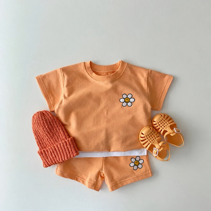 Orange daisy T-shirt and matching shorts laid out with a knit hat and sandals