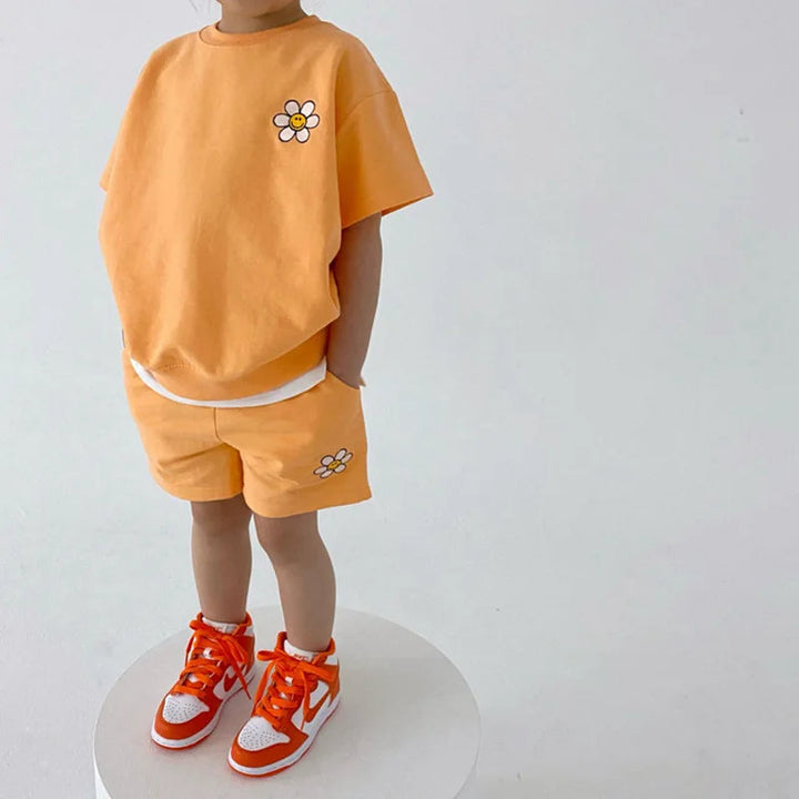 Child wearing an orange daisy T-shirt and shorts with orange sneakers