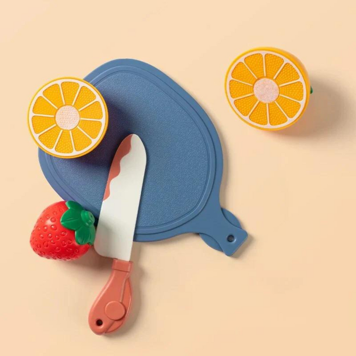 Pretend orange halves beside a strawberry, blue cutting board, and pink-handled toy knife