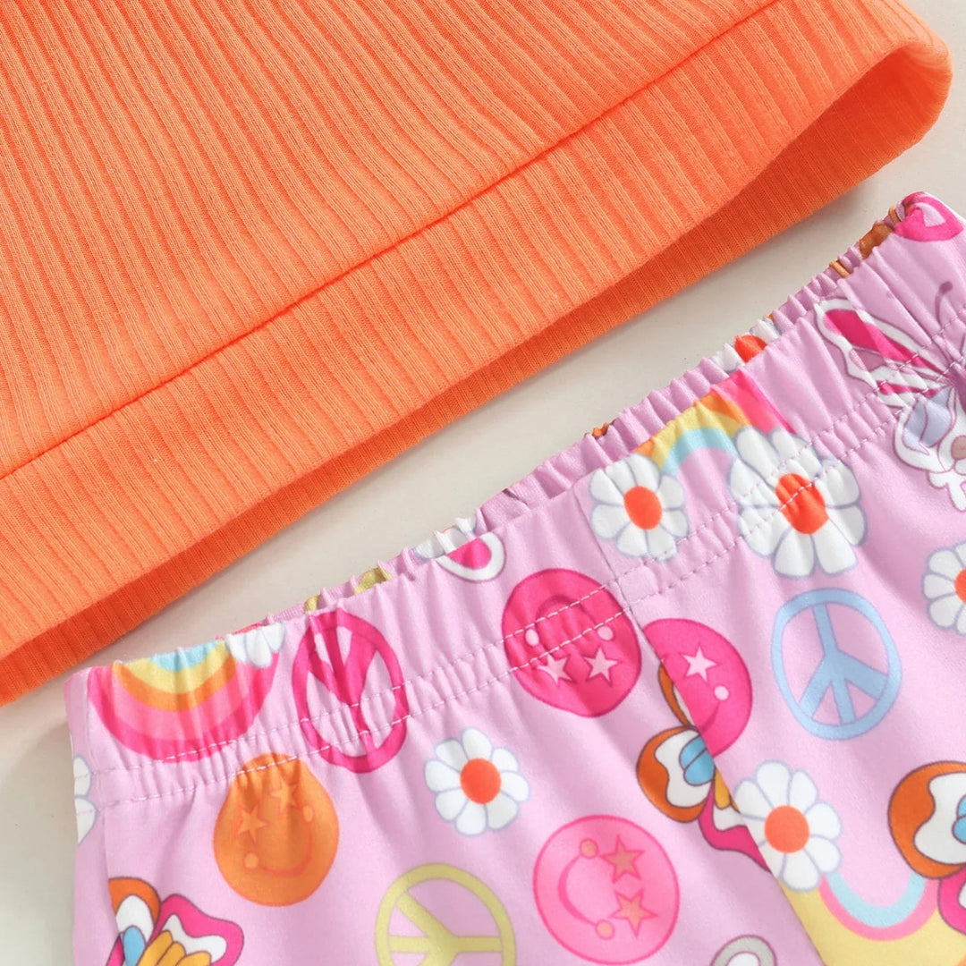 Orange ribbed top hem beside the elastic waistband of pink floral and peace-sign print pants.