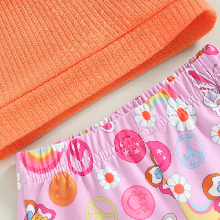 Orange ribbed top hem beside the elastic waistband of pink floral and peace-sign print pants.