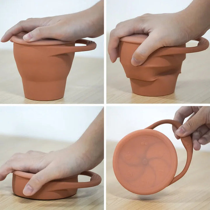 Hands pressing an orange silicone snack cup flat and carrying it by its handle