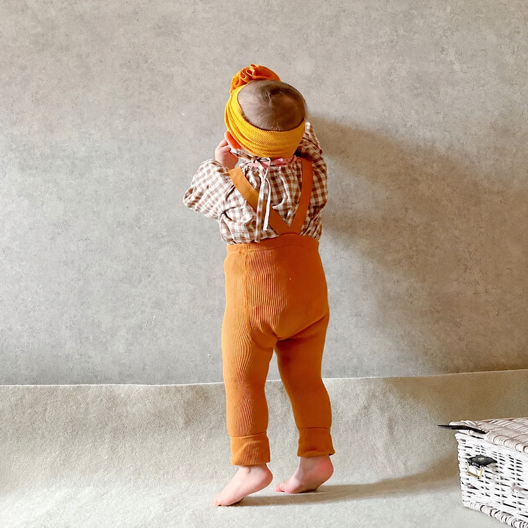 Baby wearing orange suspender leggings with a checked top