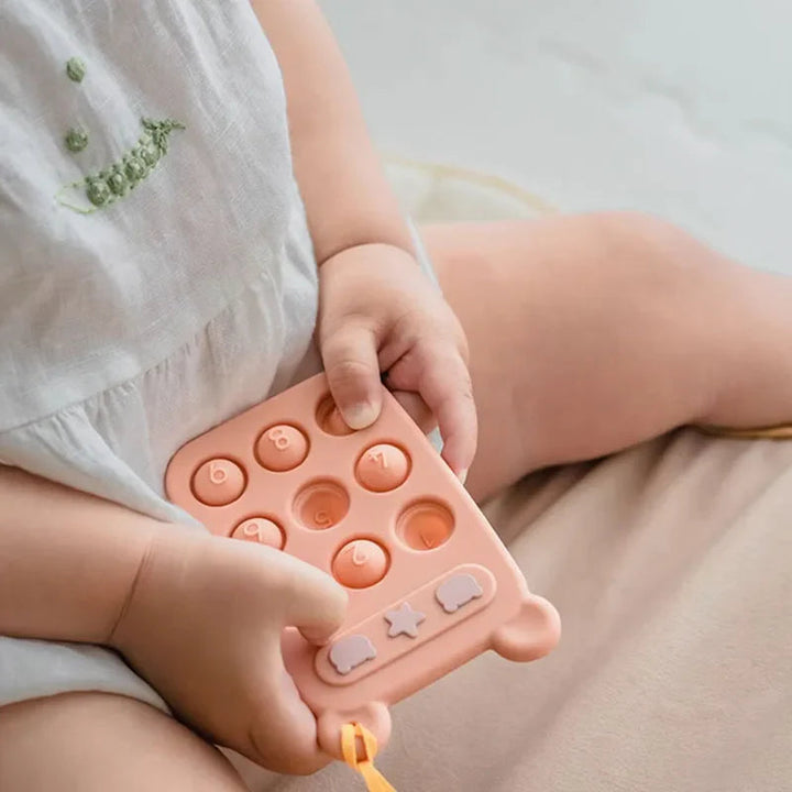 Small hands holding an orange silicone teething phone with round numbered buttons
