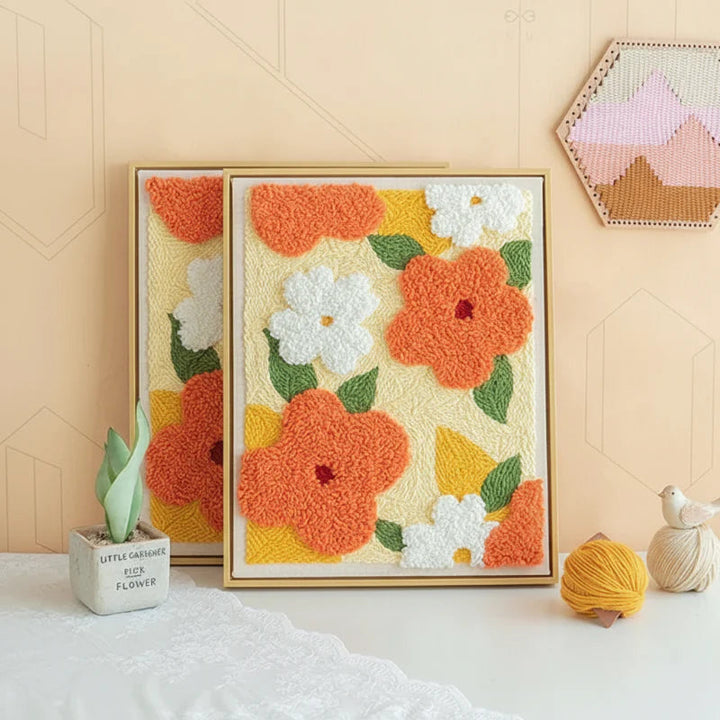 Two framed floral punch needle artworks with orange and white flowers.