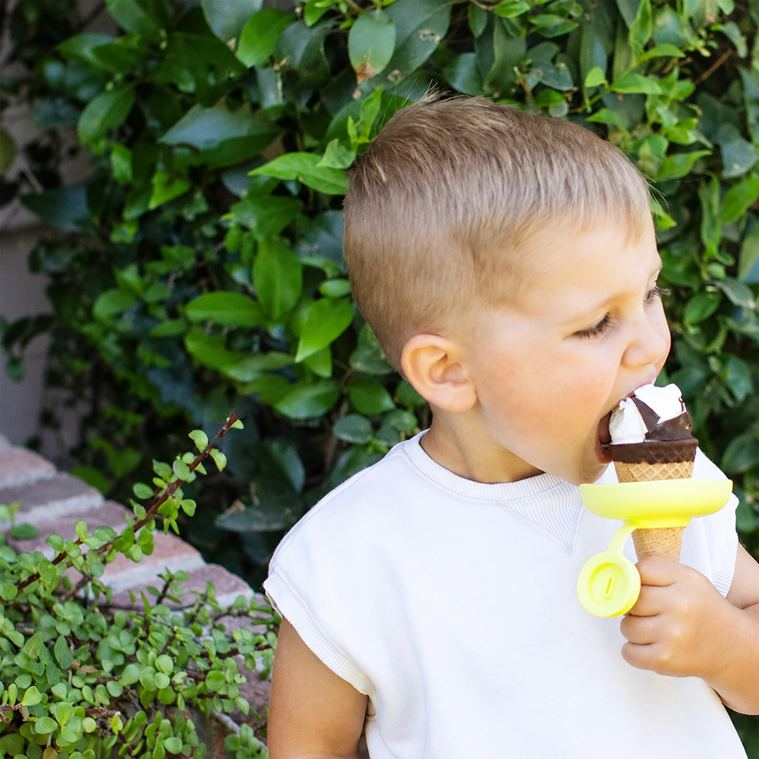 Child outdoors eating an ice cream cone with a yellow silicone holder