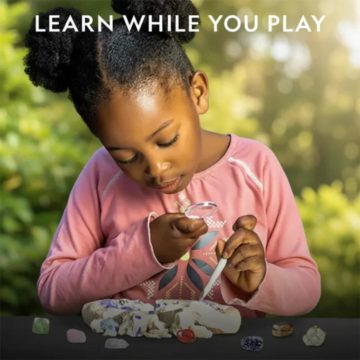 Child examining a gemstone with a magnifying glass beside an excavation block outdoors