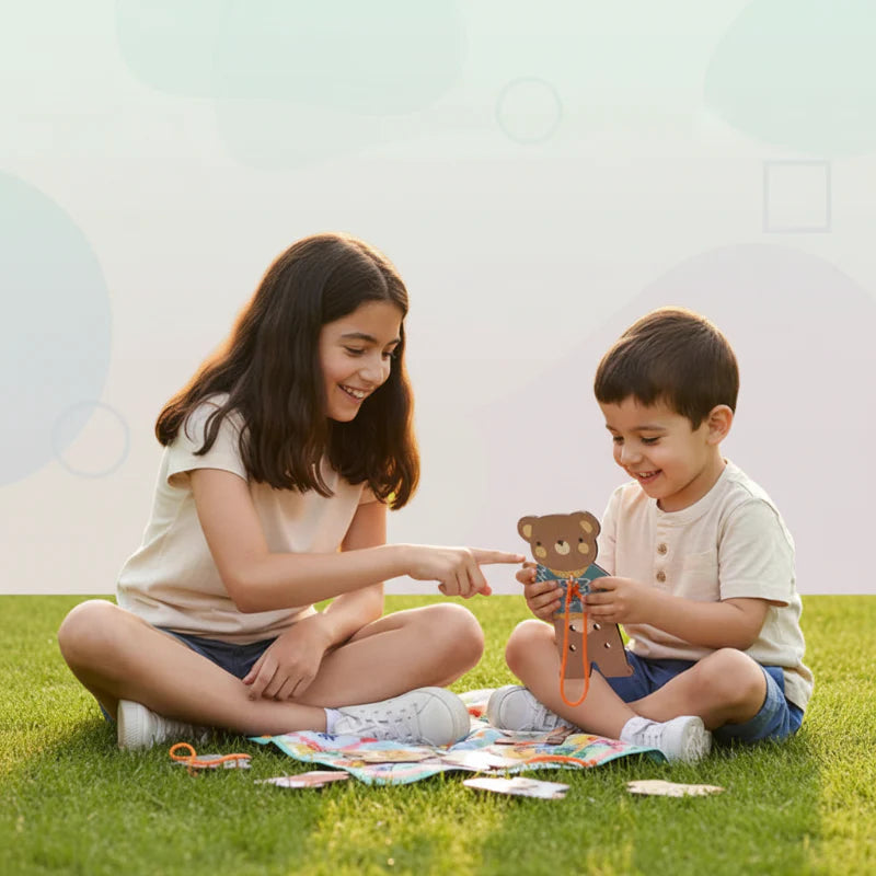An adult and child sit on the grass while threading a wooden dress-up bear.