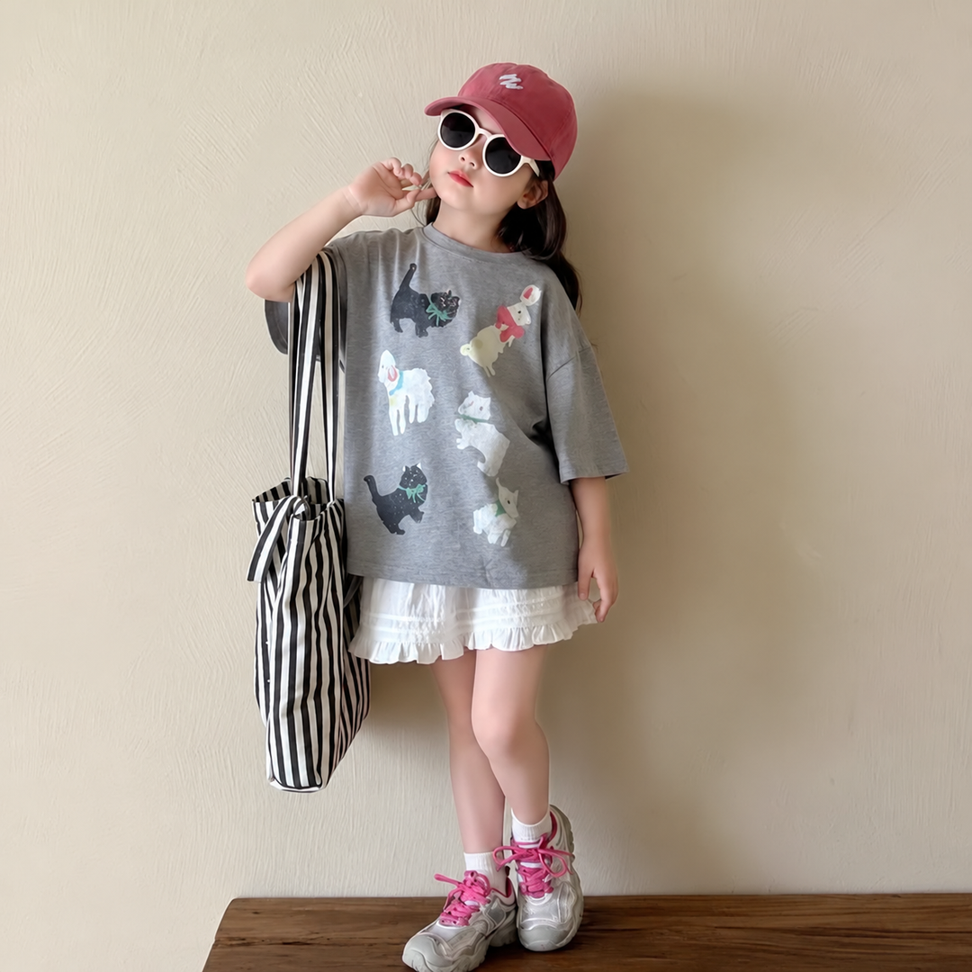Girl in an oversized cat-print T-shirt, pink cap, and sunglasses with a white skirt.
