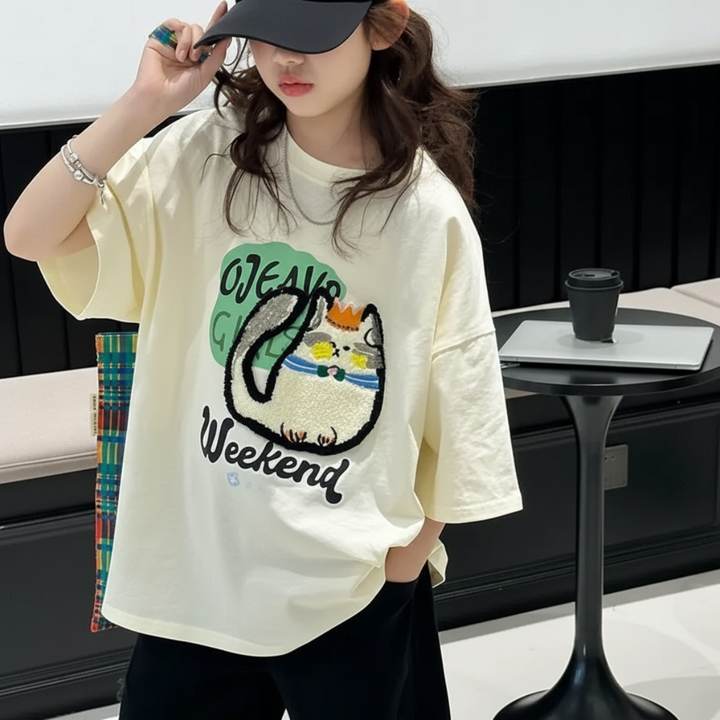 Front view of the oversized cream cat T-shirt worn with black shorts and a cap
