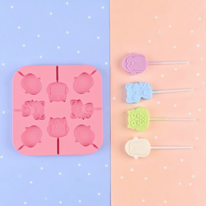 Pink lollipop mold with owl and other animal cavities beside pastel treats