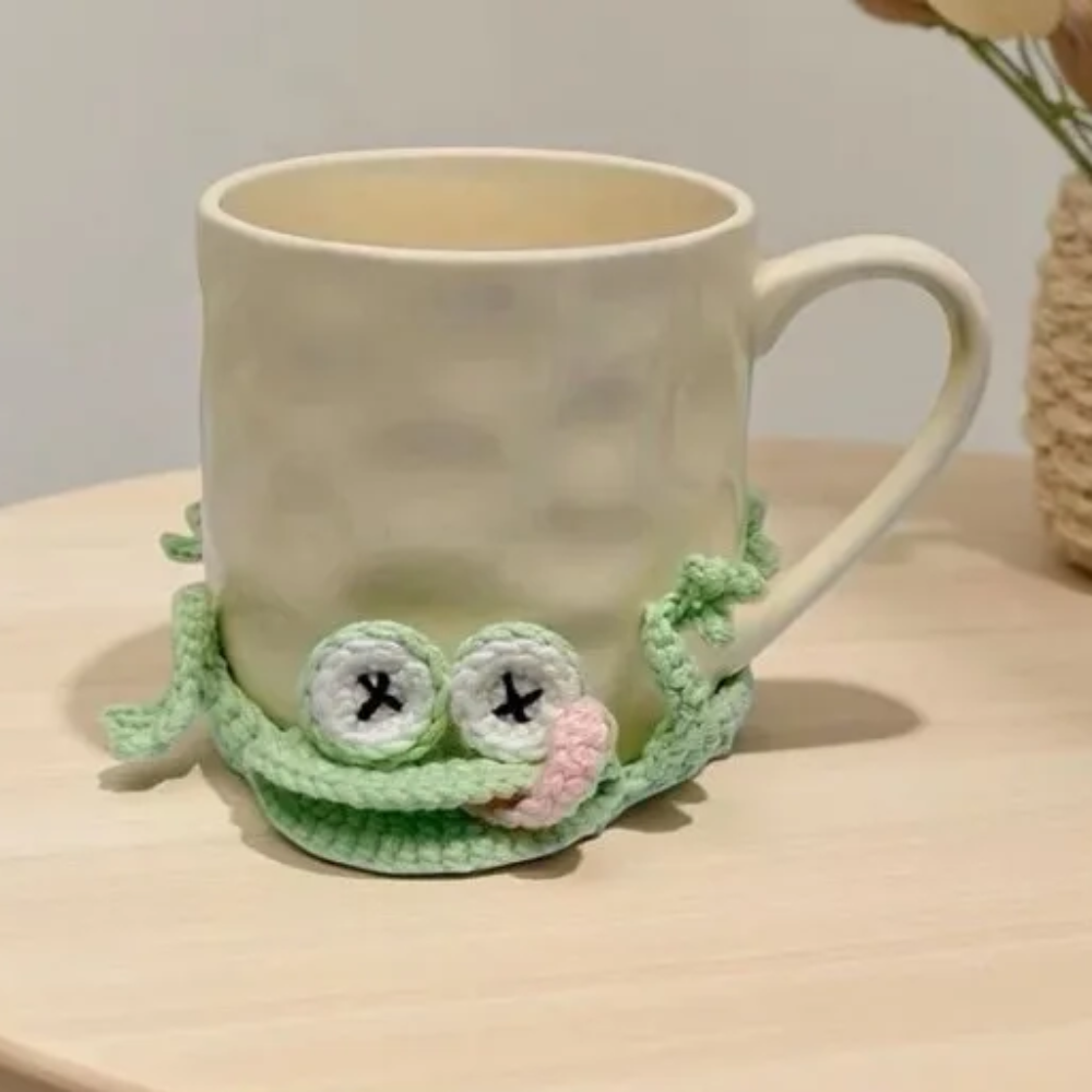 Ceramic mug resting on a pale green crocheted frog coaster with stitched eyes