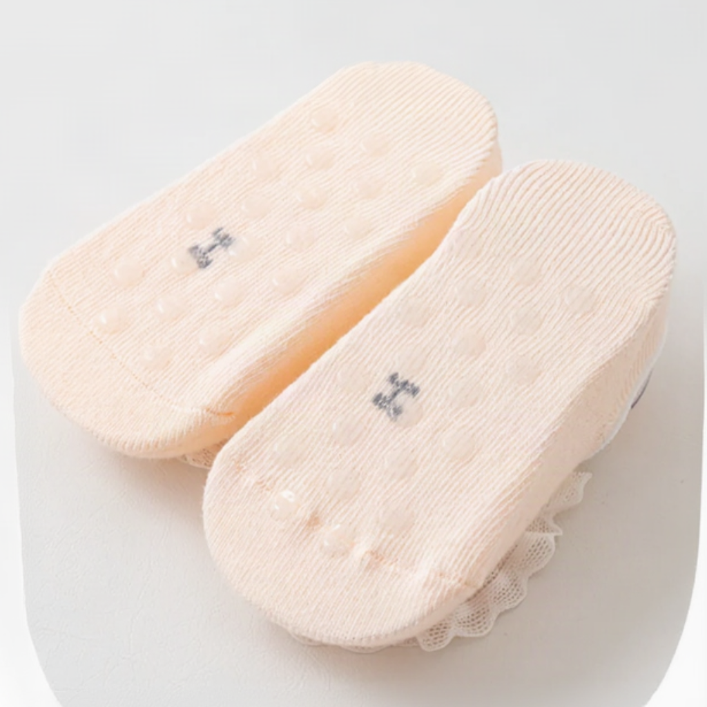 Undersides of pale pink baby socks showing small raised dots on the soles