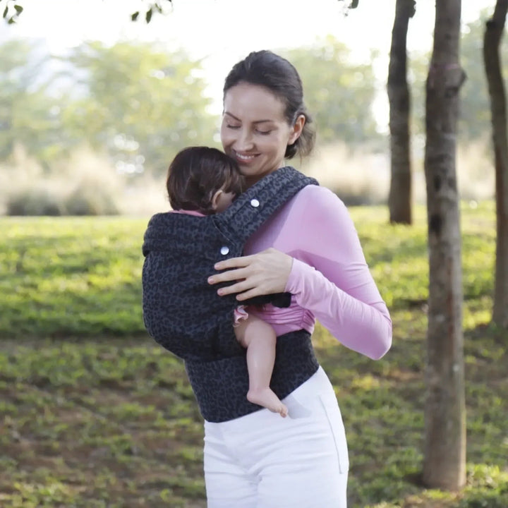 Parent looking down at a baby in a dark leopard-print carrier during an outdoor walk