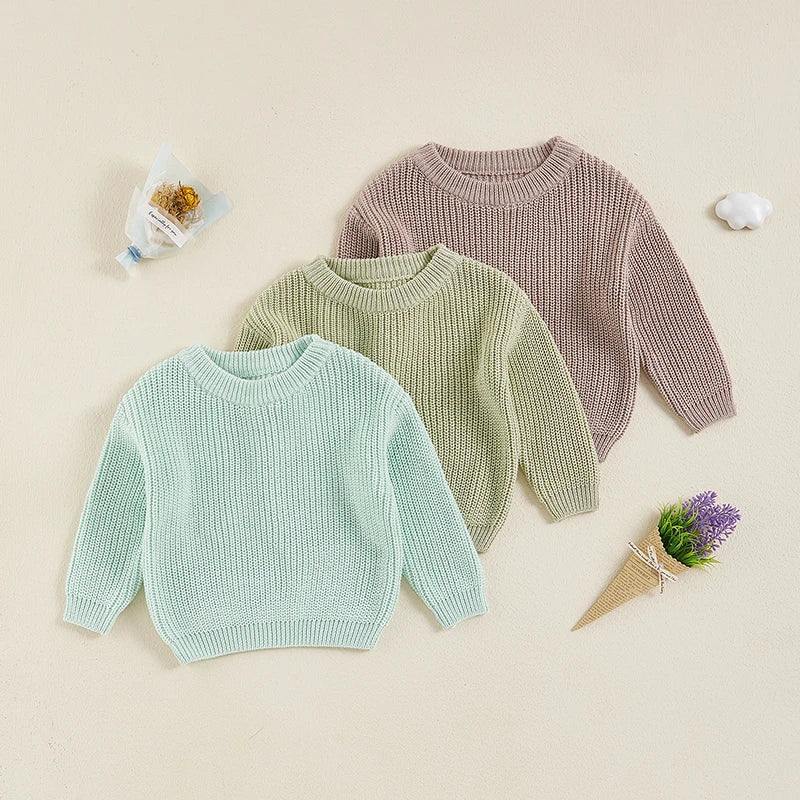 Three children's knit sweaters in pastel colors with round necklines, long sleeves, and ribbed trim.