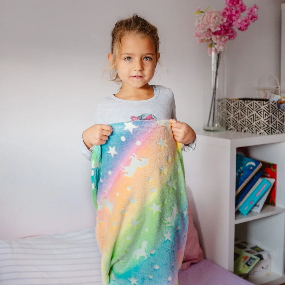 Child holding a pastel rainbow mermaid sleeping bag with star and unicorn prints.