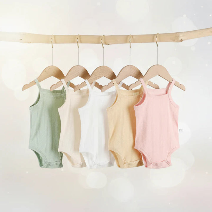 Pastel baby bodysuits with thin shoulder straps hanging from wooden hangers