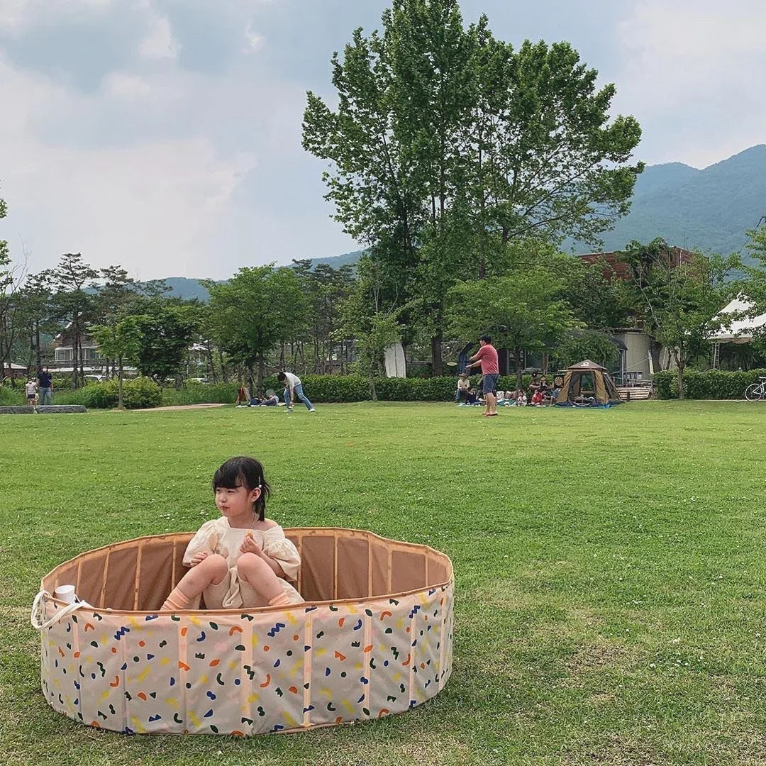 Child sitting in a round patterned play pool on a grassy lawn