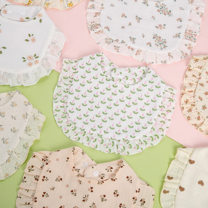 Ruffled baby bibs with floral, tulip, and heart prints arranged on pastel backgrounds