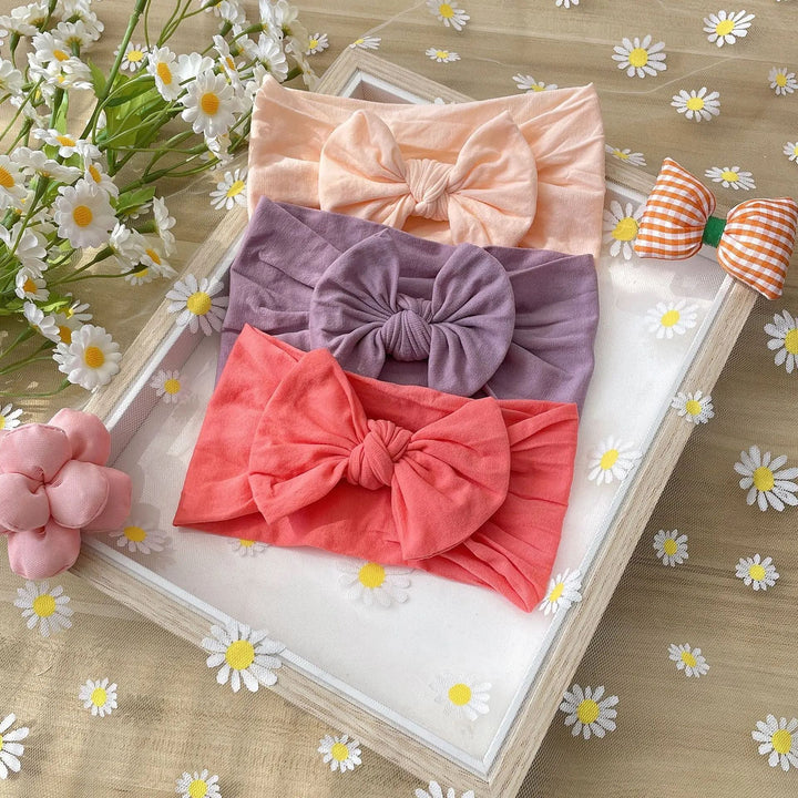 Peach, muted purple, and coral bow headbands arranged in a frame