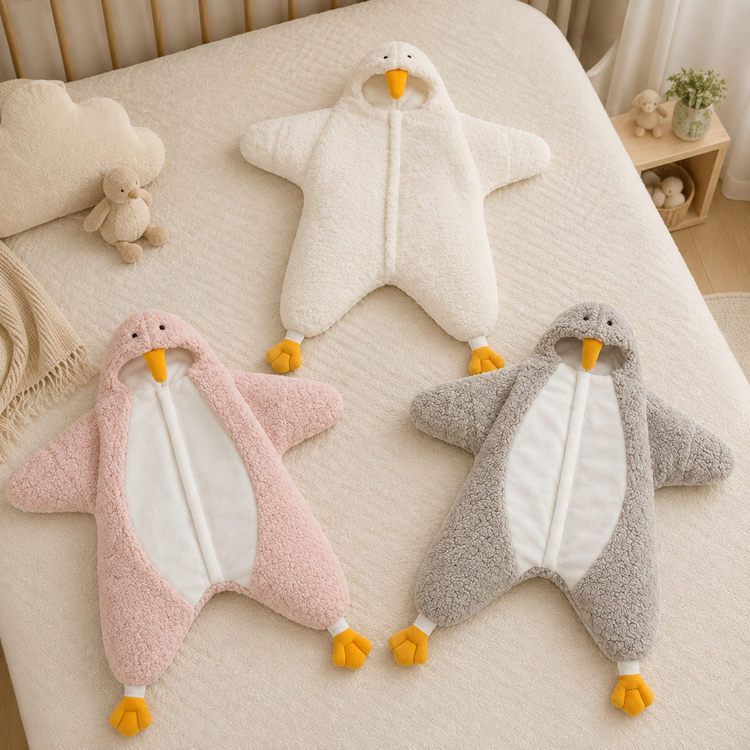 White, pink, and gray penguin baby jumpsuits with yellow beaks and feet arranged on a bed