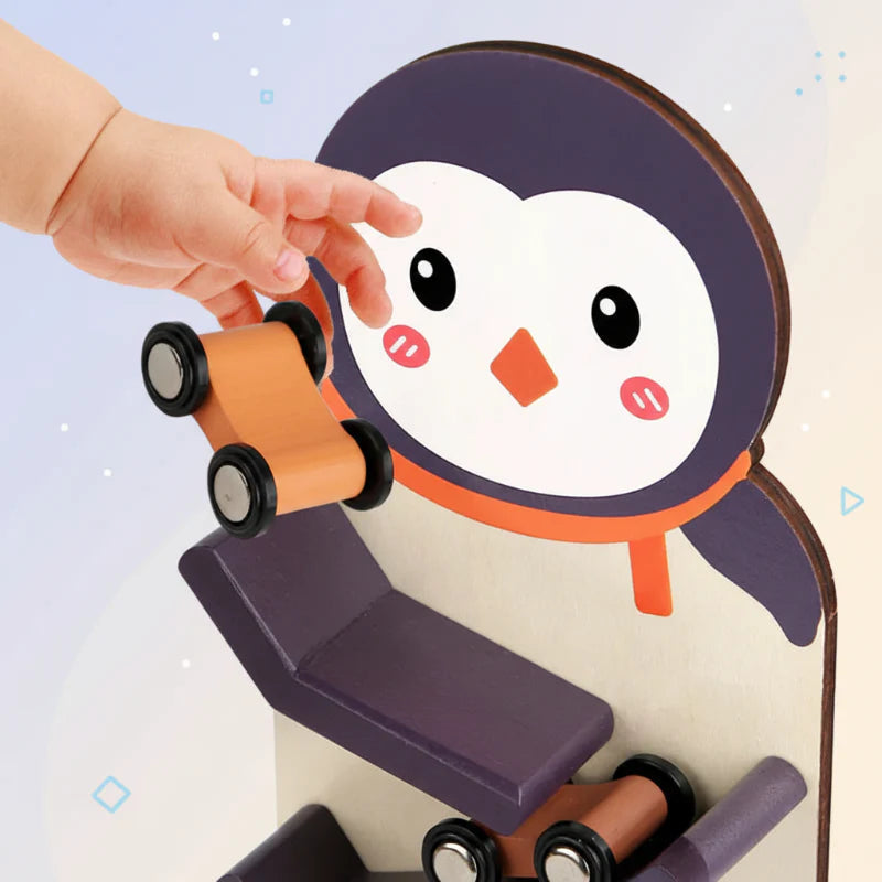 A hand holds an orange wooden car above the top ramp of the penguin track