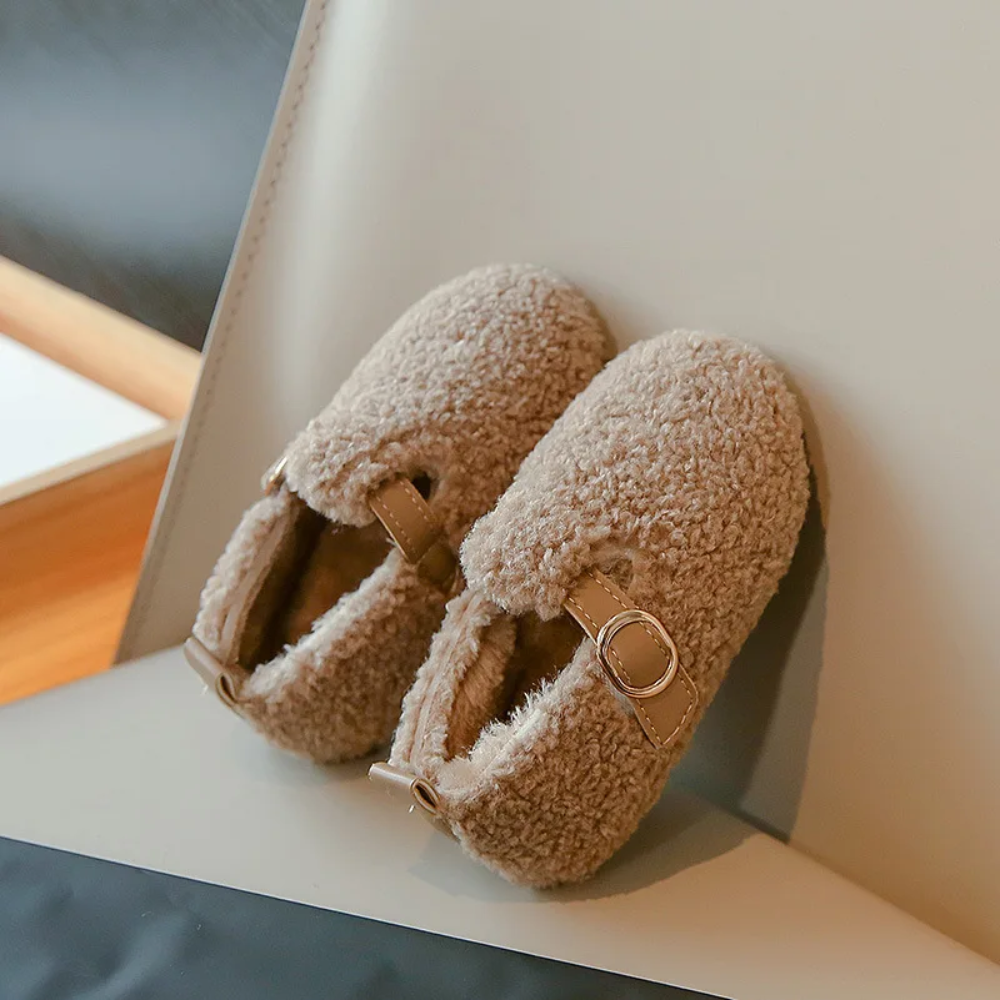 Persimmon plush winter shoes with buckle details resting on a chair