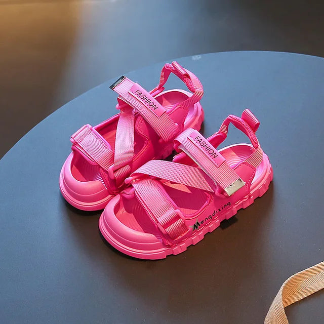 Pink sandals on a table, showing adjustable straps and textured soles.