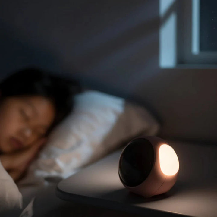 Pink alarm clock casting a warm bedside glow beside a sleeping child