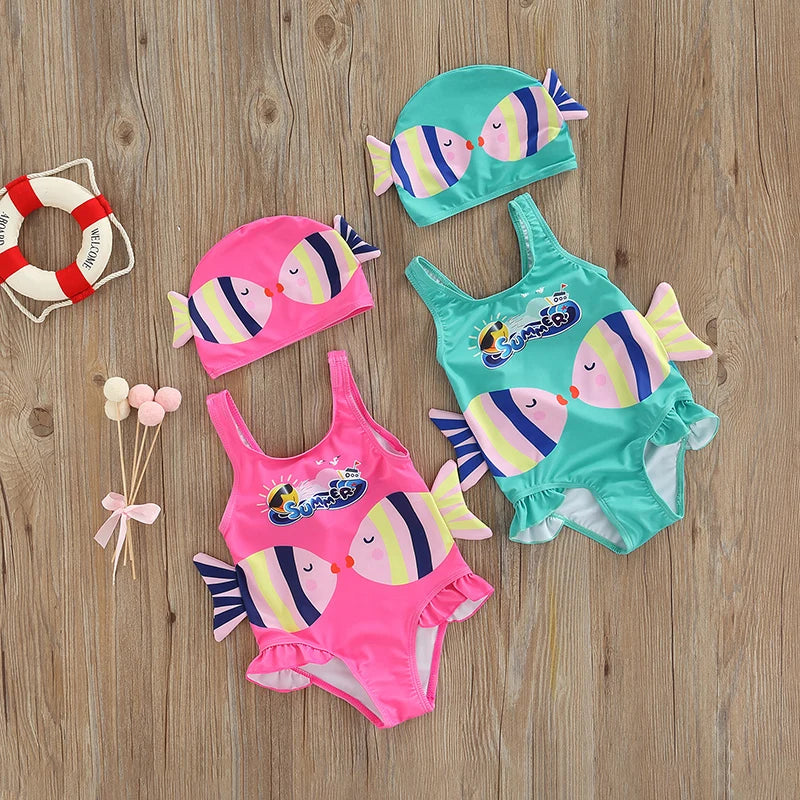 Pink and blue fish-print one-piece swimsuits with matching swim caps on a wood background