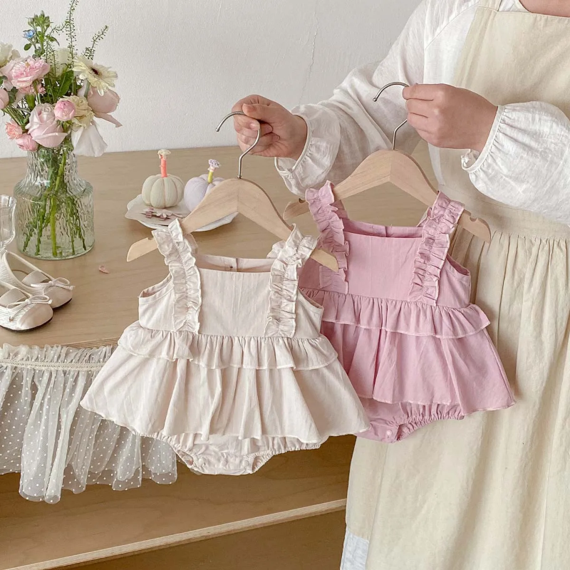 Pink and apricot baby dress rompers held on wooden hangers