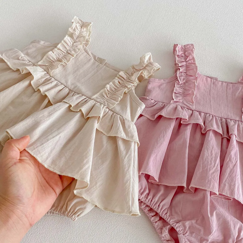 Close-up of apricot and pink dress rompers showing ruffled waists and layered skirt overlays