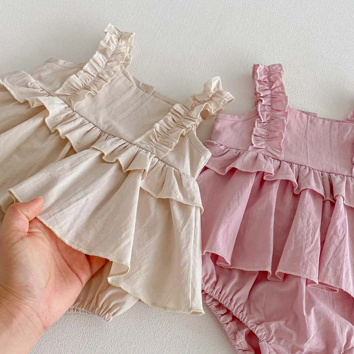 Close-up of apricot and pink dress rompers showing ruffled waists and layered skirt overlays
