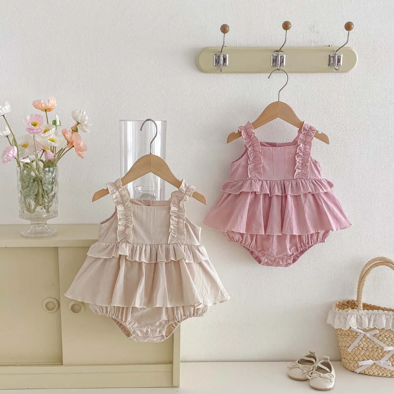 Pink and apricot ruffle baby dress rompers hanging side by side on a wall rack