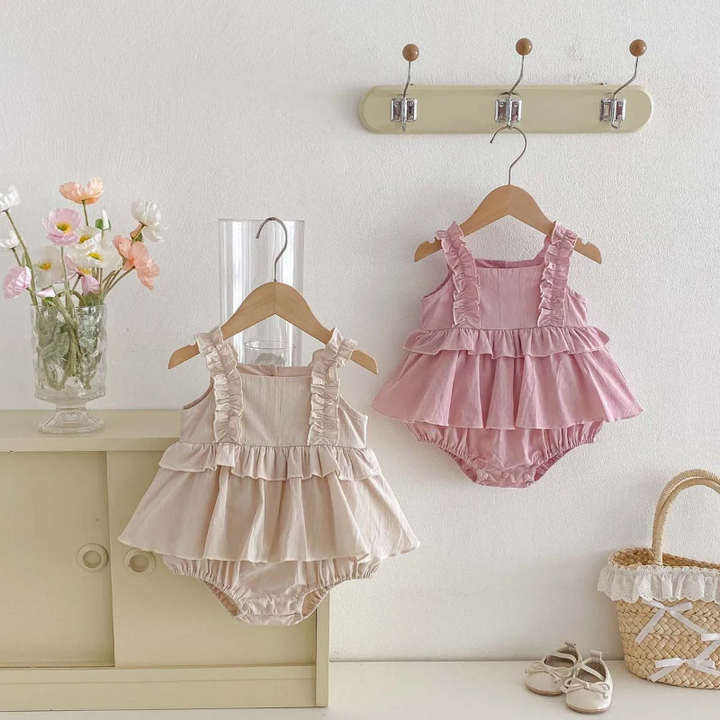 Pink and apricot ruffle baby dress rompers hanging side by side on a wall rack