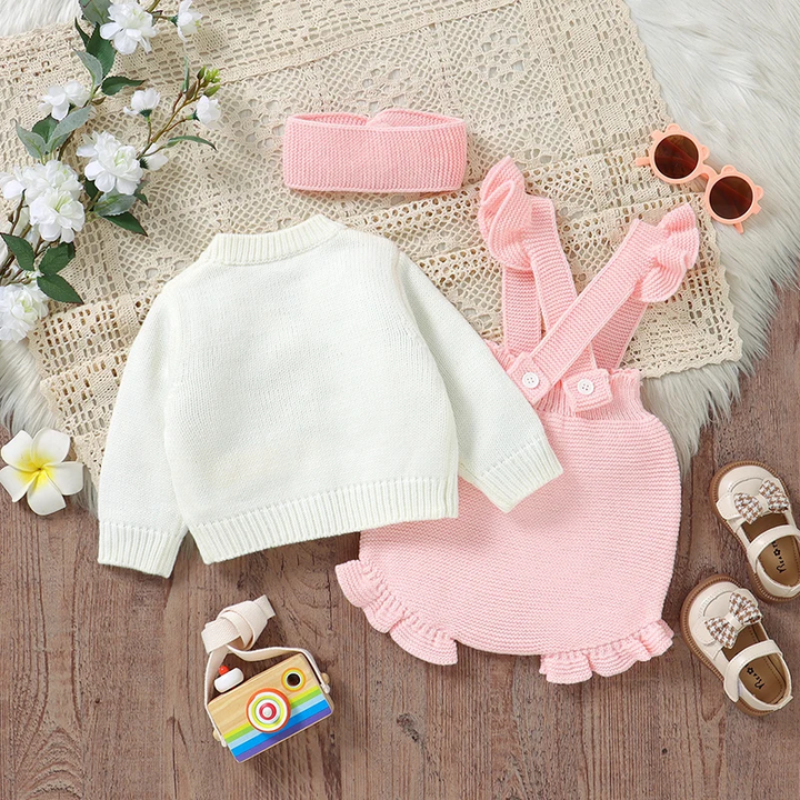 Back of the white knit cardigan beside pink overalls and a matching headband