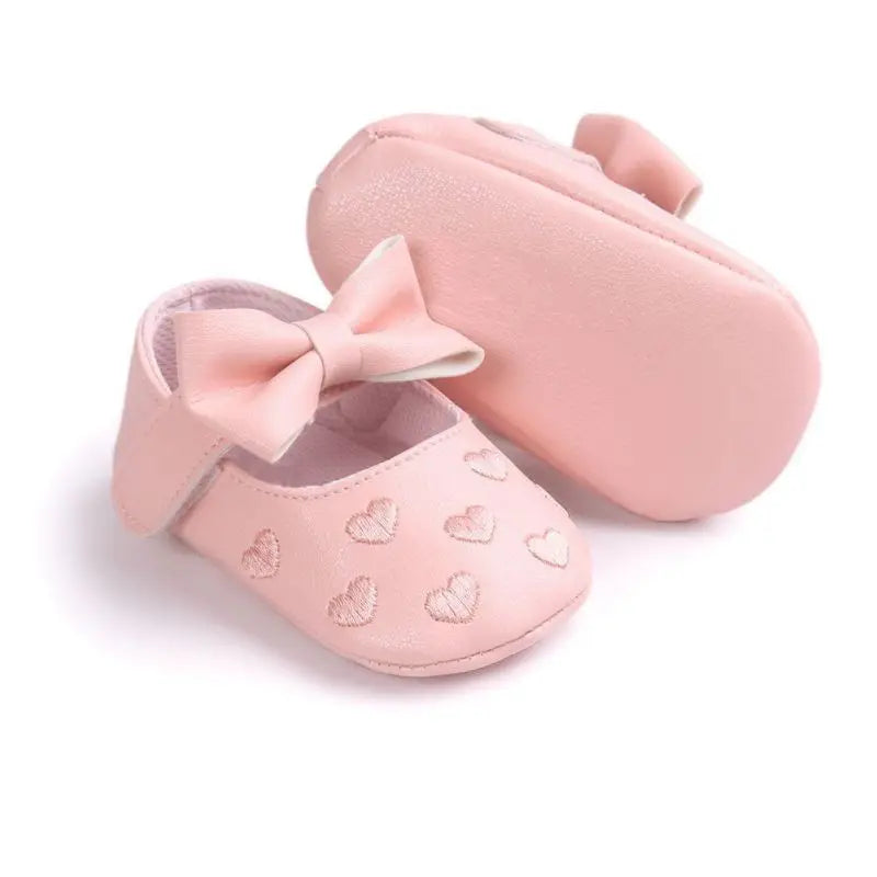 Pink bow baby shoes showing the sole of one shoe and the front of the other