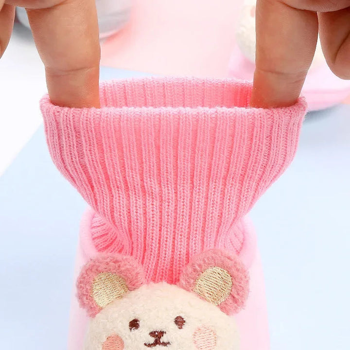 Pink baby slipper with its ribbed knit collar stretched open by hand