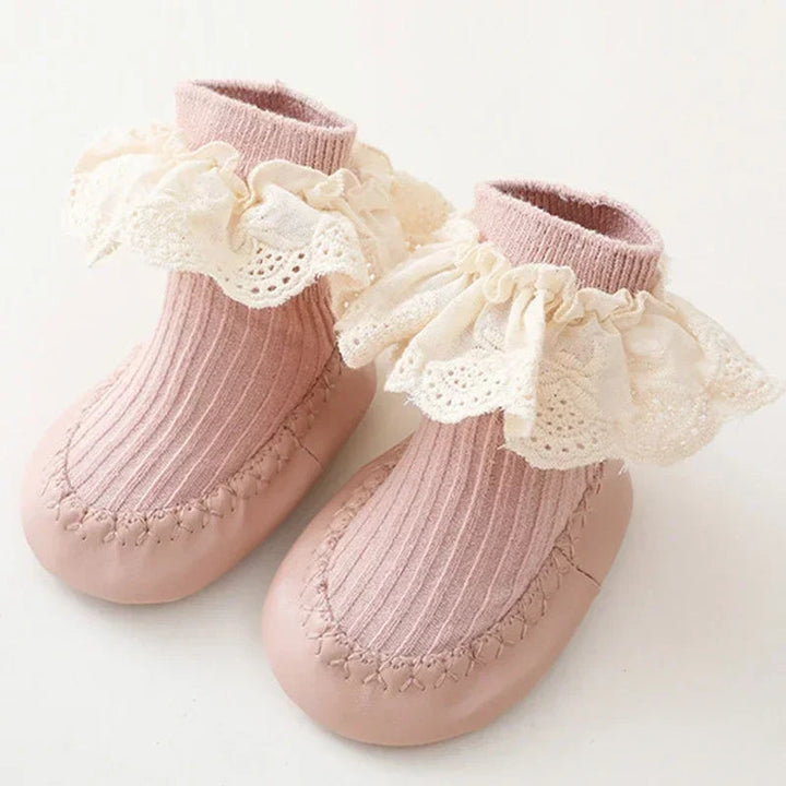 Pink baby sock shoes with ribbed uppers, rounded toes, and cream lace ruffles